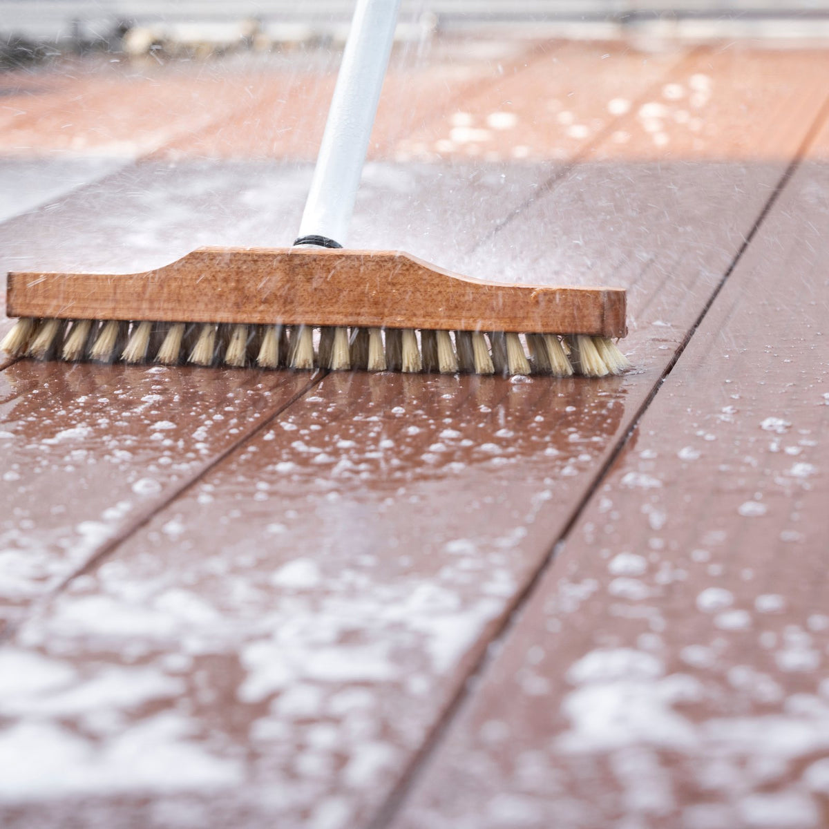 Scrubbing a wet wooden deck with a stiff deck brush